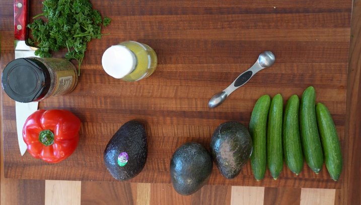 Overhead view of cutting board that has avocados, peppers and cucumbers that will be a made into a salad.