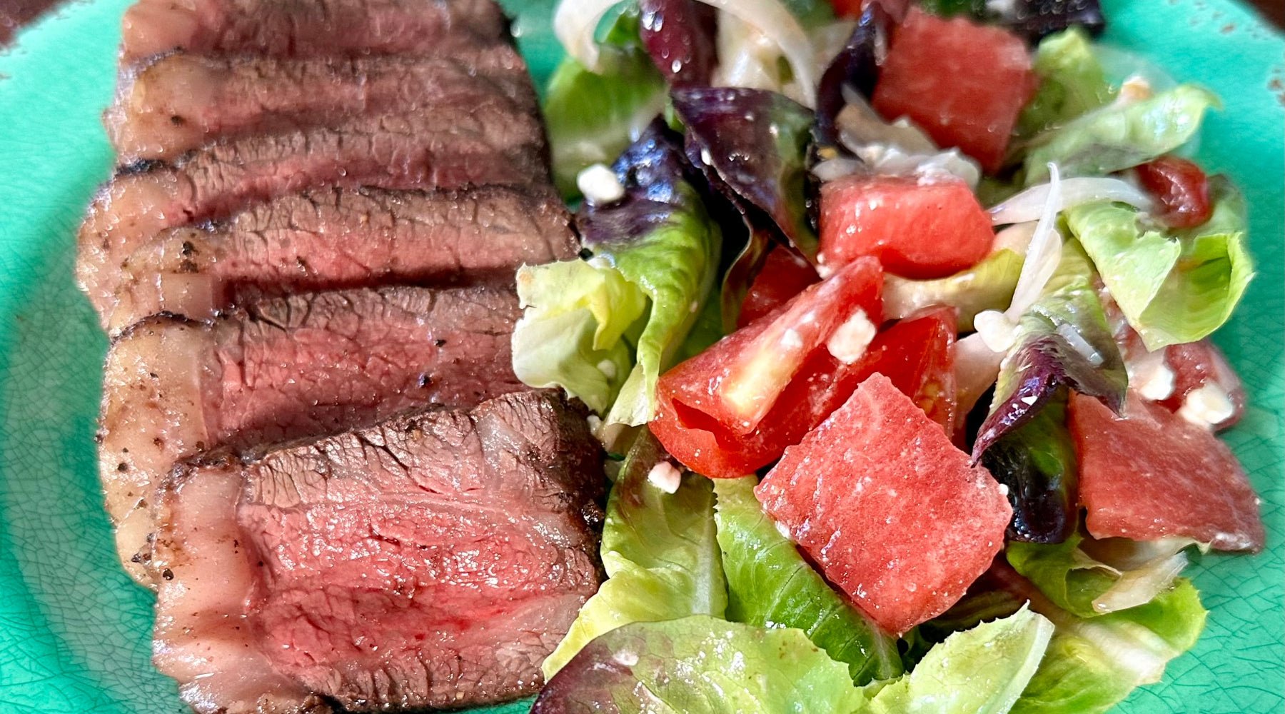 Sliced Wagyu Picanha steak served with a fresh salad of lettuce, tomatoes, and feta cheese on a green plate.