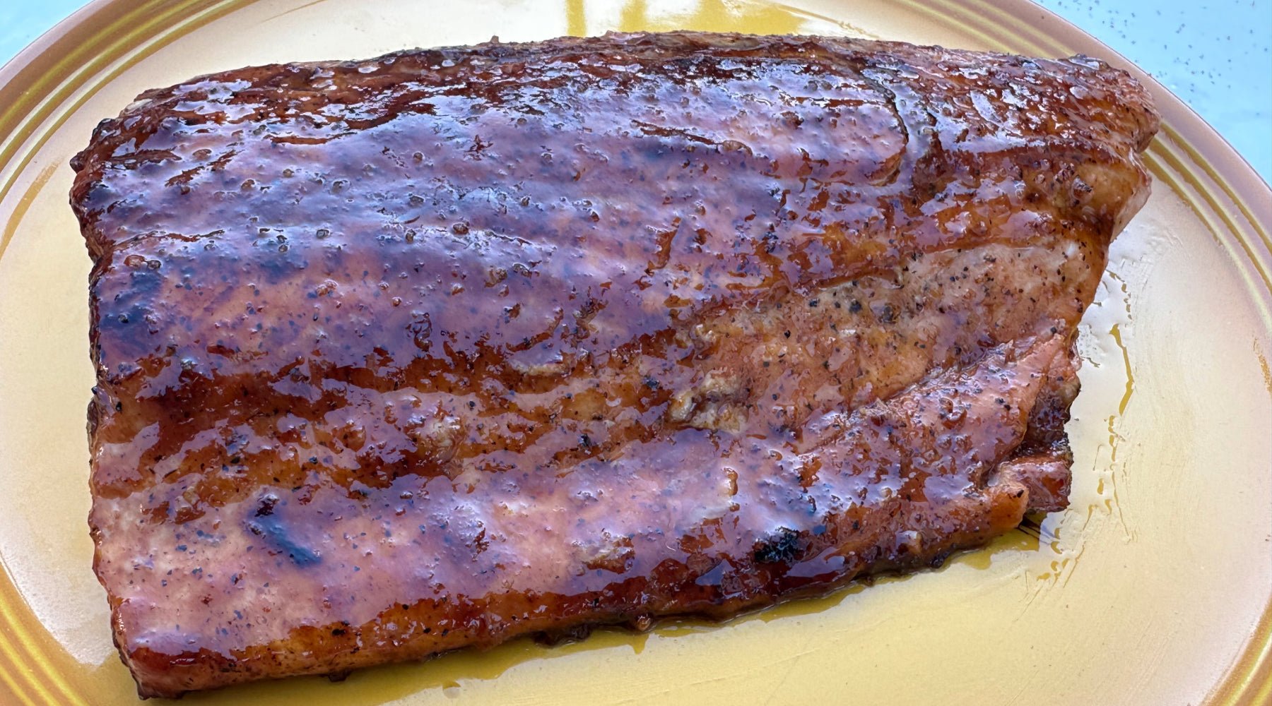 A glazed piece of salmon with a shiny, caramelized surface, served on a yellow plate with visible juices.