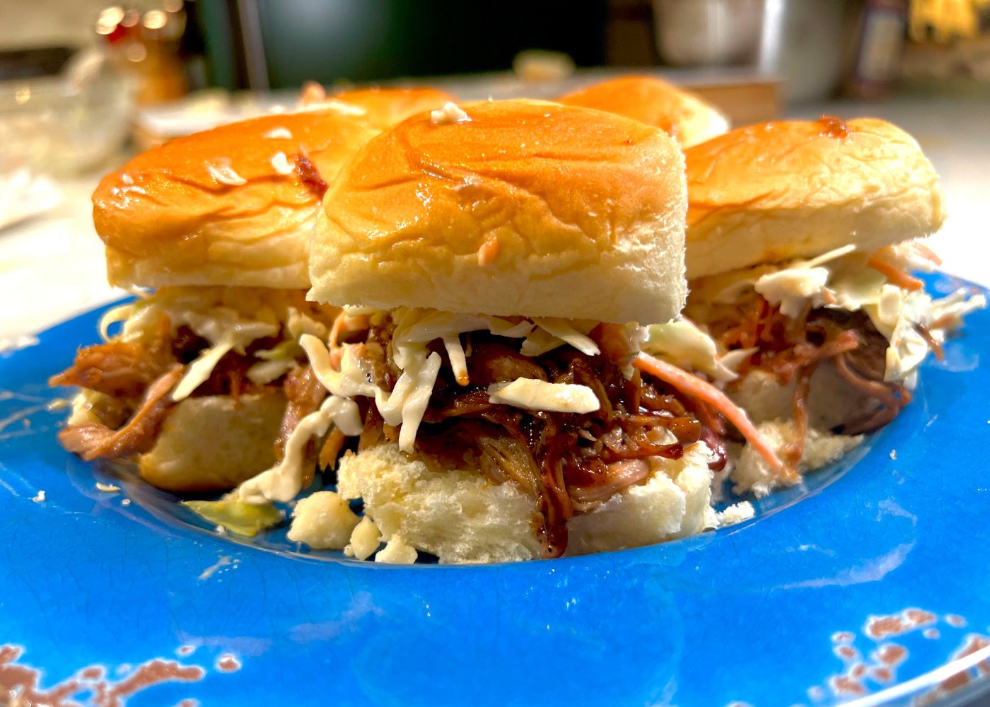 Pulled pork sliders with miso macadamia slaw on glossy buns, served on a vibrant blue plate.