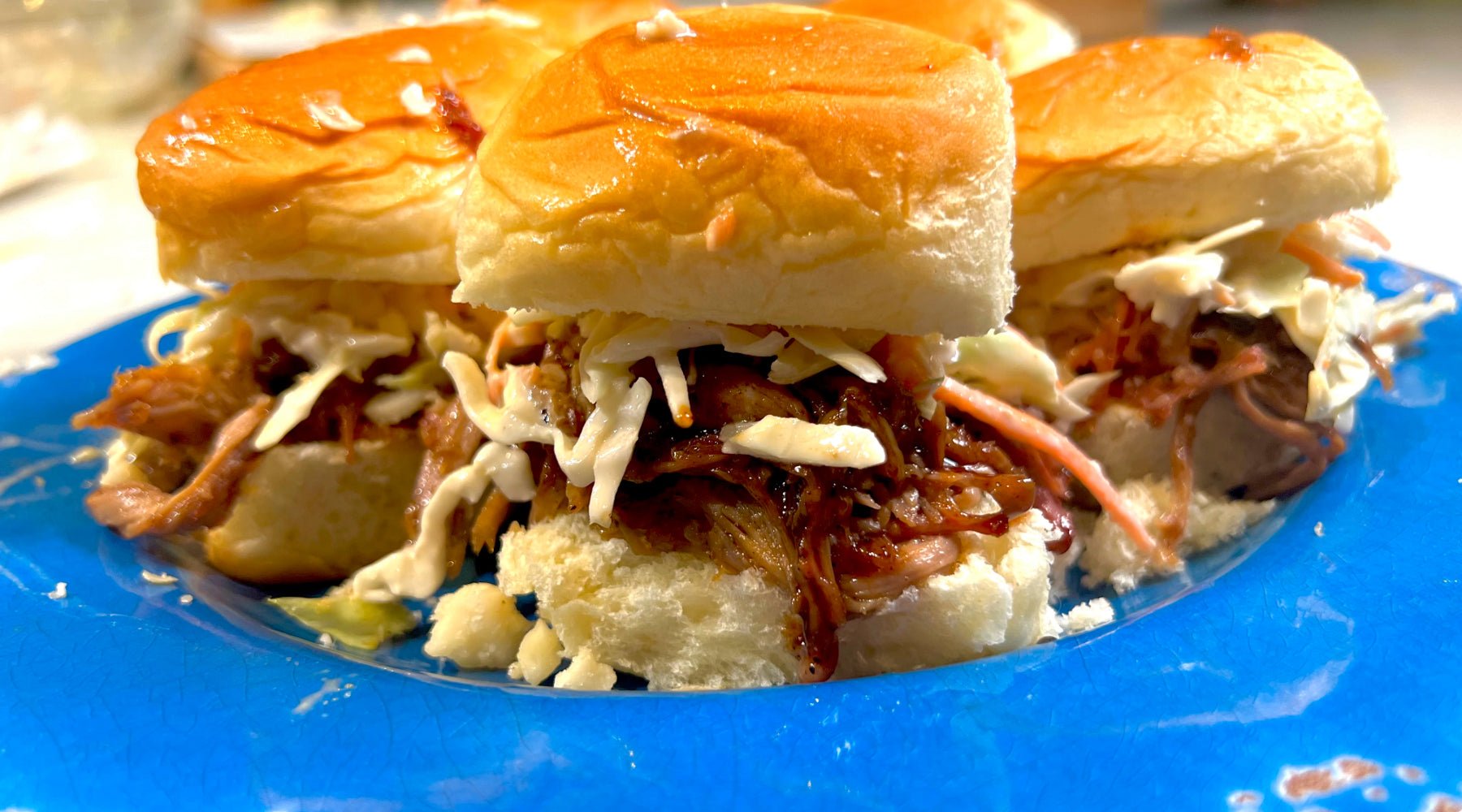 Pulled pork sliders with miso macadamia slaw on glossy buns, served on a vibrant blue plate.