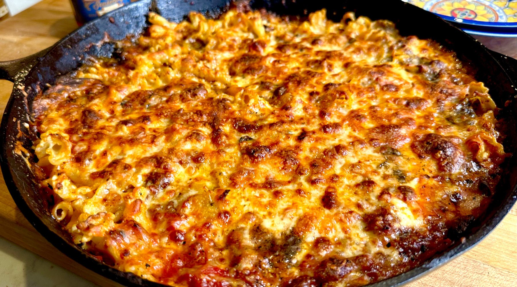 A cast iron skillet filled with baked pasta topped with melted, golden-brown cheese and a bubbling tomato-based sauce.