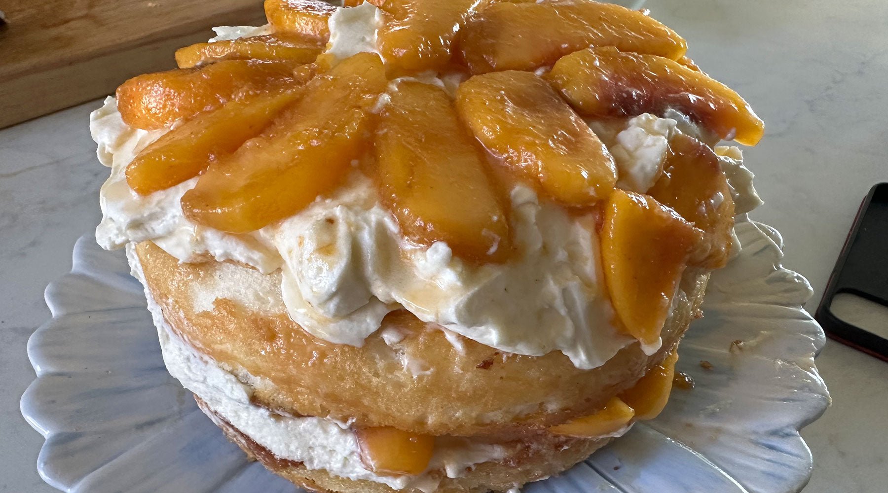 Beautiful multi layer angel food cake with grilled peaches covering the top and whip cream and peaches between the layers.