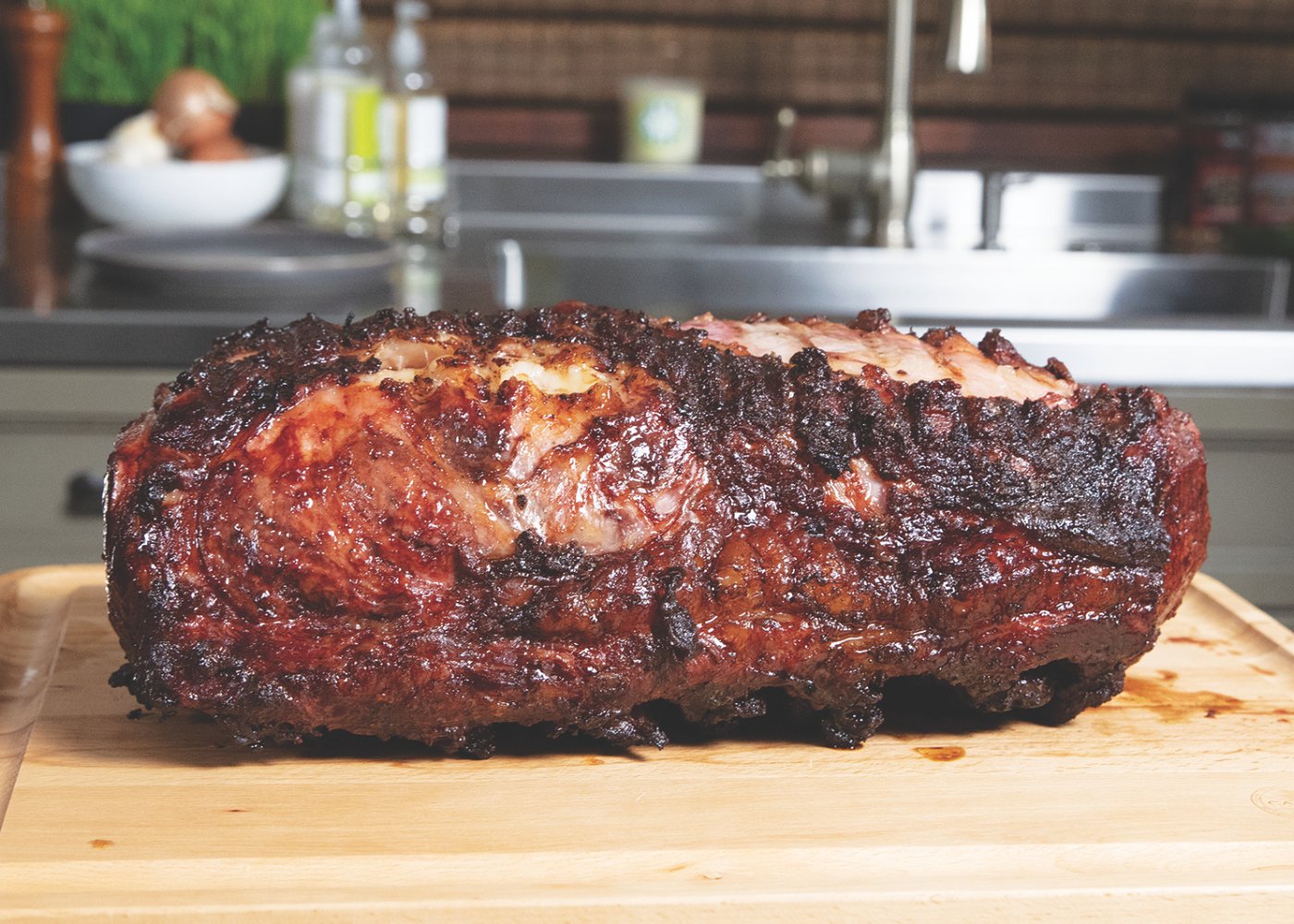 A perfectly cooked prime rib roast with a crispy, golden-brown crust and juicy, marbled interior resting on a wooden cutting board in a kitchen setting.