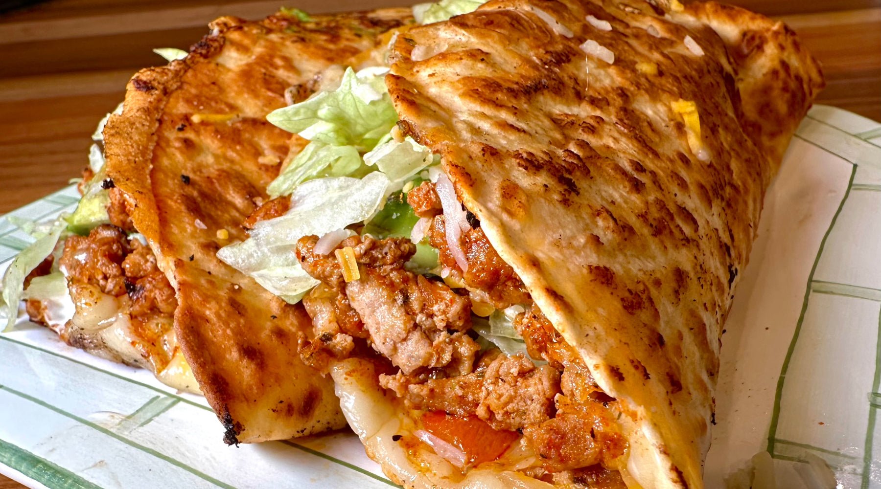 Grilled turkey quesataco filled with melted cheese, seasoned meat, lettuce, and onions on a white plate.