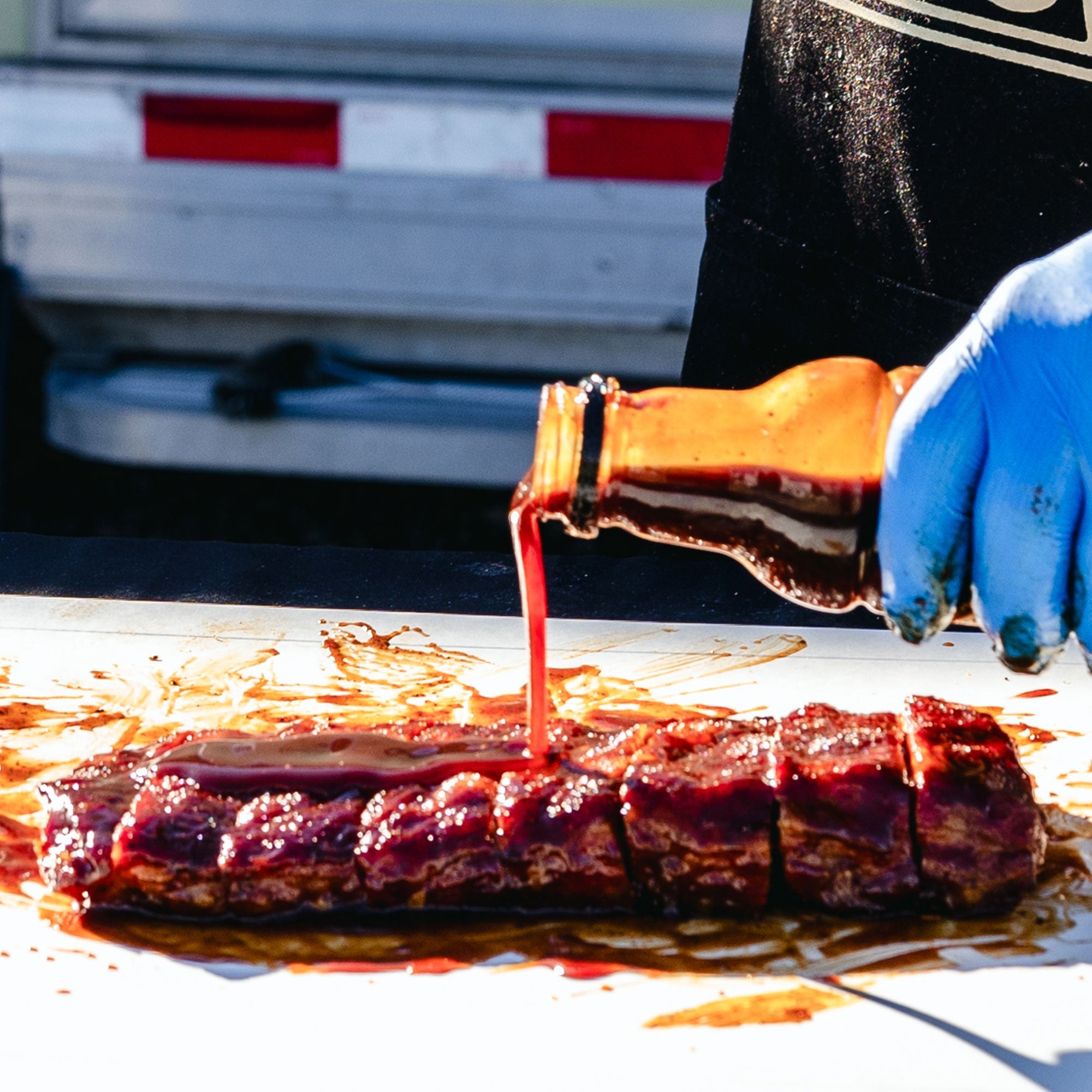 Big Poppa pouring Granny's BBQ Sauce over the top of a slab of ribs that is dripping in sauce.