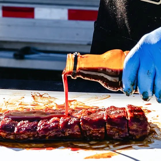 Big Poppa pouring Granny's BBQ Sauce over the top of a slab of ribs that is dripping in sauce.