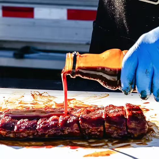 Big Poppa pouring Granny's BBQ Sauce over the top of a slab of ribs that is dripping in sauce.