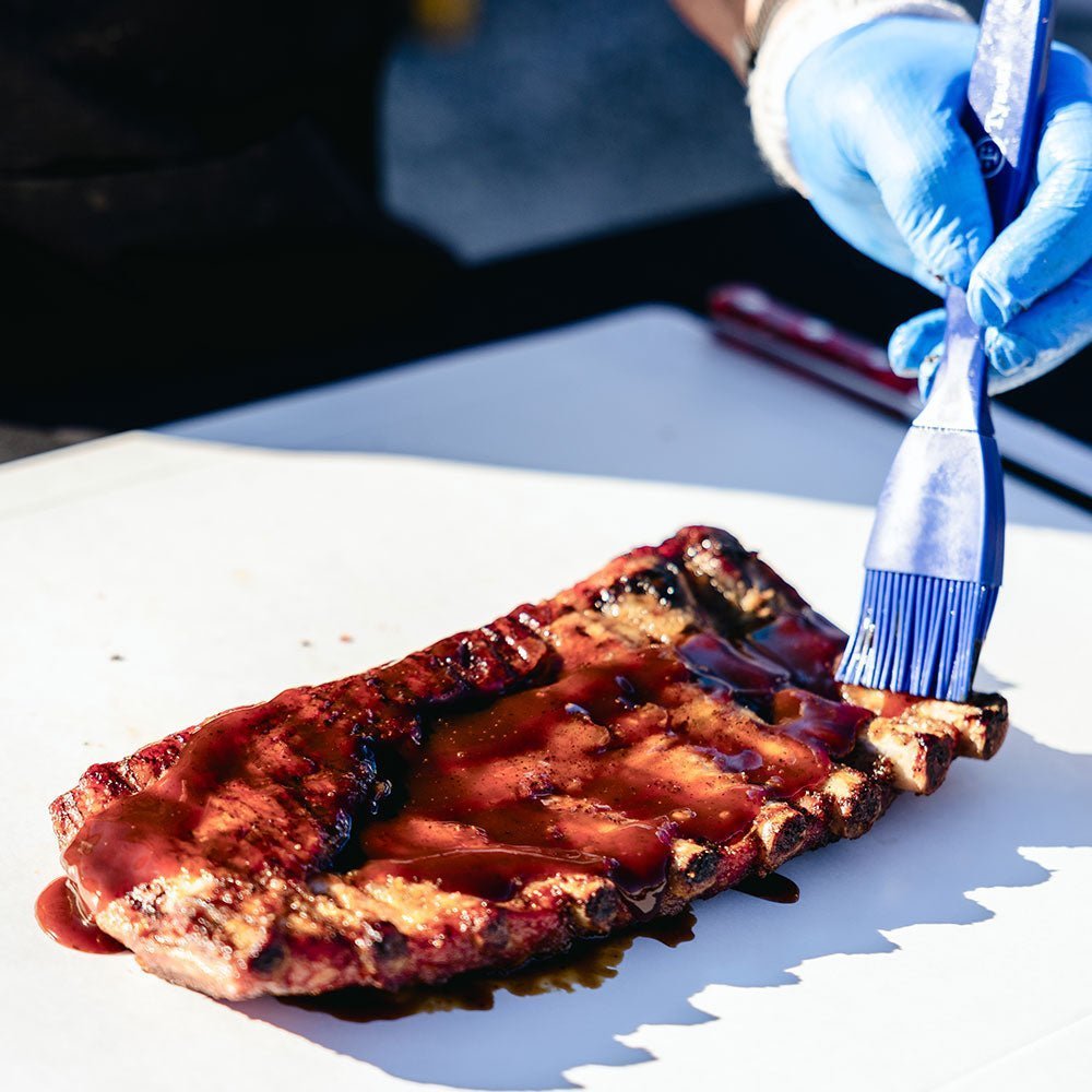Big Poppa pouring Granny's BBQ Sauce on a slab of ribs.