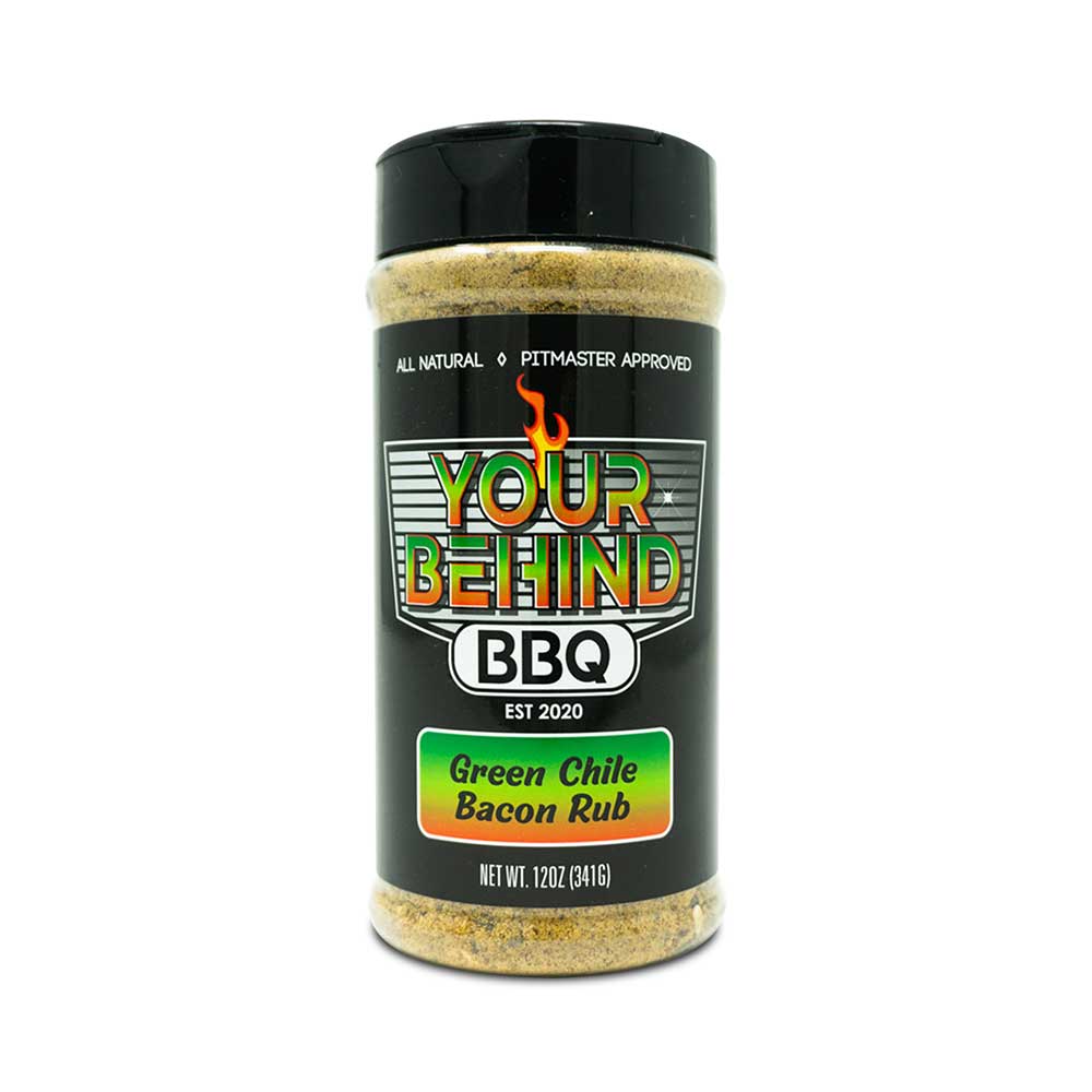 Jar of 'Your Behind BBQ Green Chile Bacon Rub.' The black jar features a colorful label with 'Your Behind BBQ' in bold letters, indicating it is all-natural and pitmaster approved. The label also reads 'Green Chile Bacon Rub' and 'Net Wt. 12oz (341g).