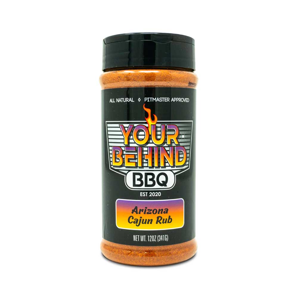 Jar of 'Your Behind BBQ Arizona Cajun Rub.' The black jar features a colorful label with 'Your Behind BBQ' in bold letters, indicating it is all-natural and pitmaster approved. The label also reads 'Arizona Cajun Rub' and 'Net Wt. 12oz (341g).