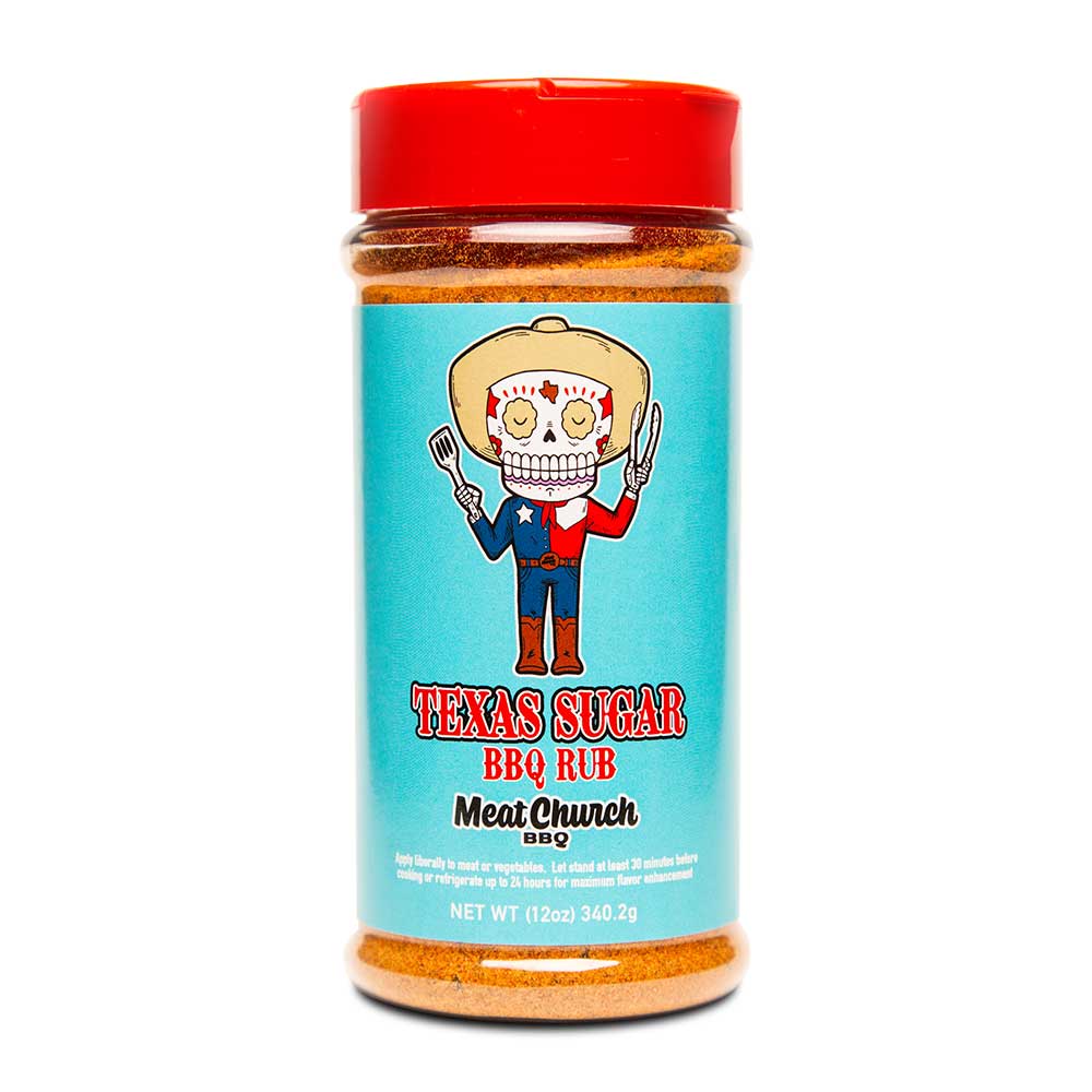 A 12-ounce jar of Meat Church Texas Sugar BBQ Rub. The label is light blue with red and white text, featuring a cartoon sugar skull dressed as a cowboy holding a fork and tongs. The jar has a red lid and contains a coarse, orange spice mix.