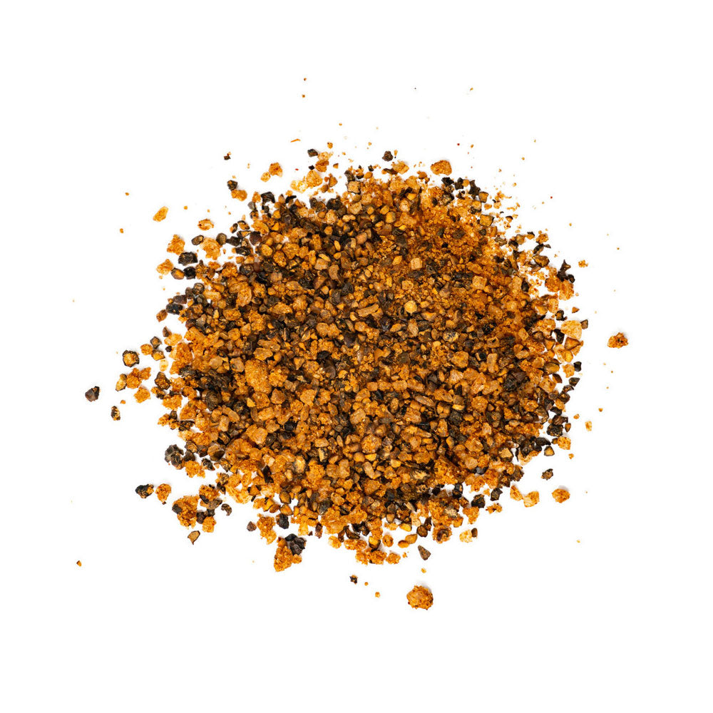 A close-up view of a pile of coarse seasoning blend, featuring black and orange-brown granules on a white background.