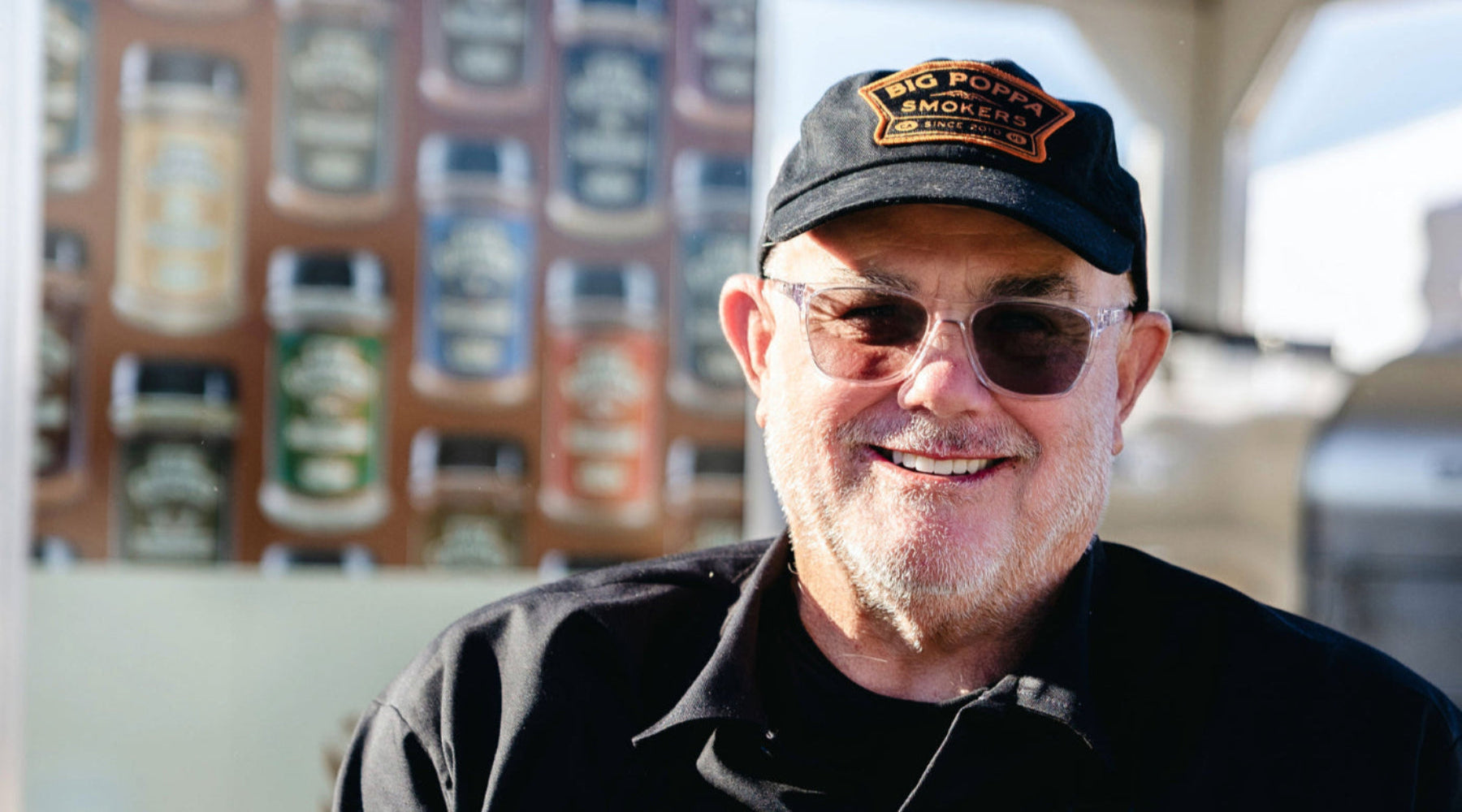 Sterling wearing a cap and sunglasses with a building featuring various signs in the background