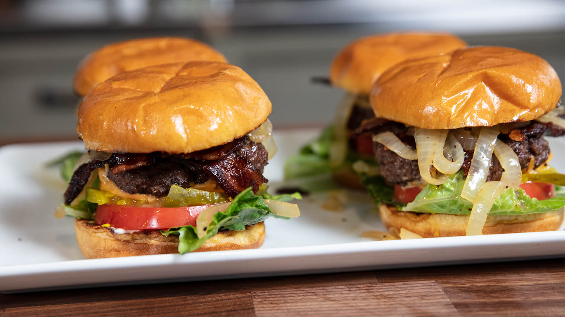 Two burgers with lettuce, tomato, and onions on a white plate.