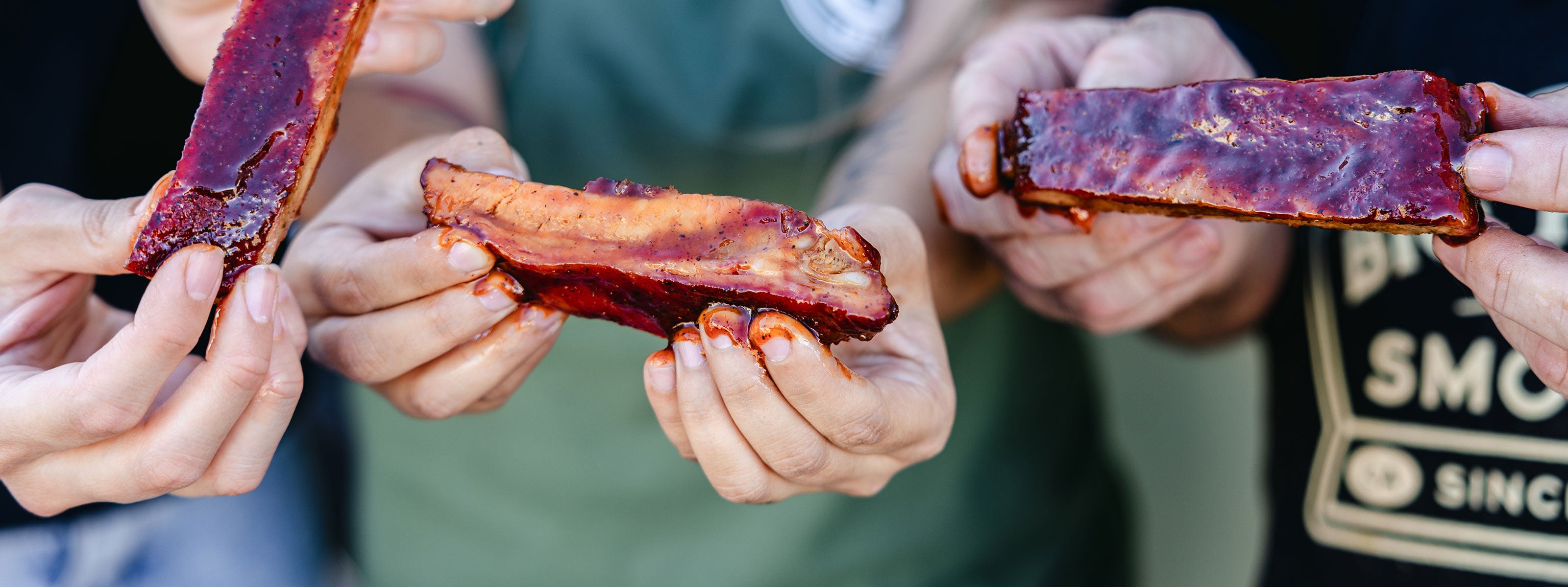 Three people eating ribs with sauce dripping off their fingers.