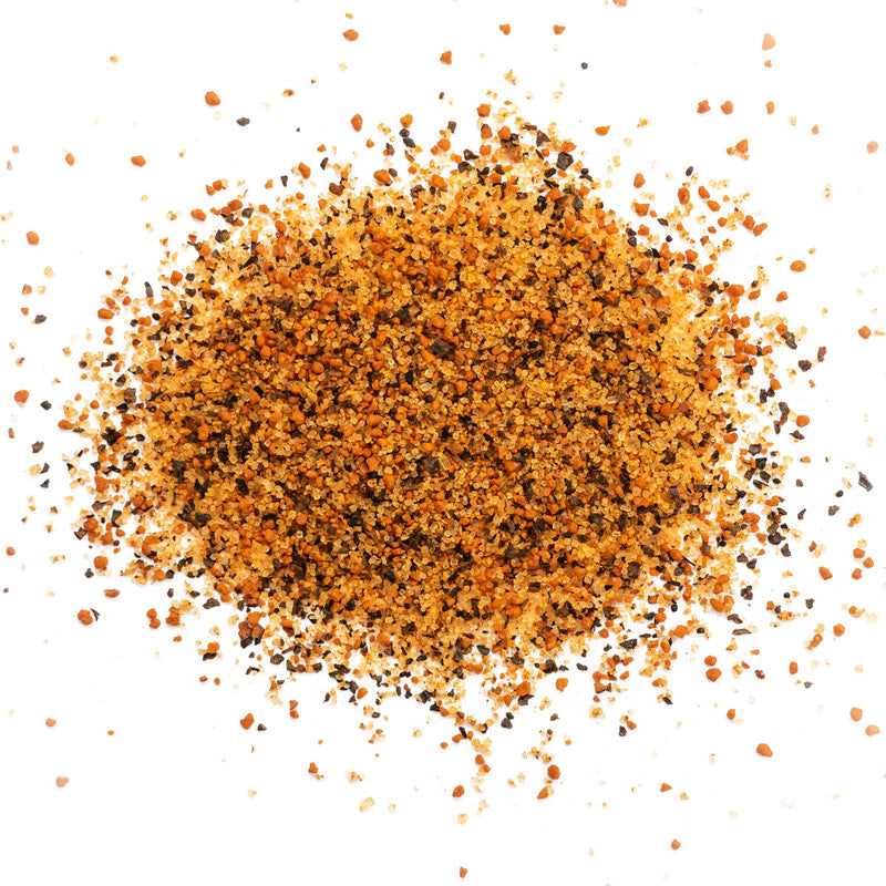 A close-up of a pile of coarse, orange-brown seasoning with visible black pepper flakes scattered on a white background.