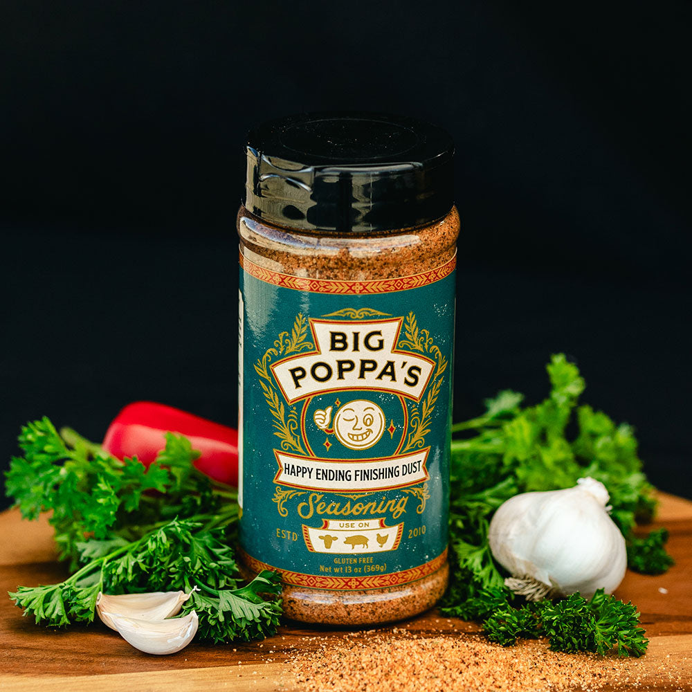 A bottle of 'Big Poppa's Happy Ending Finishing Dust' seasoning surrounded by fresh vegetables including red bell peppers and parsley, on a dark background, emphasizing the seasoning’s culinary use.