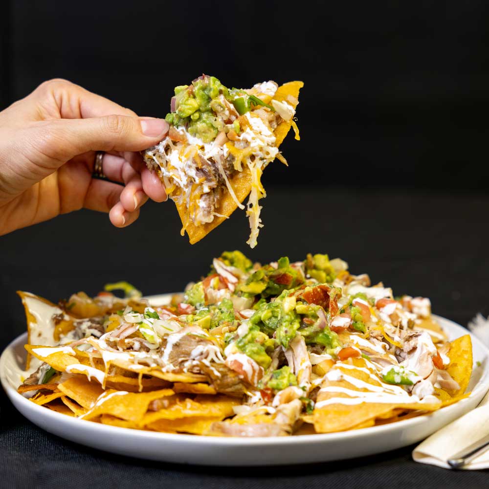 closeup of hand grabbing cheesy nacho chip seasoned with jallelujah lime barbecue seasoning