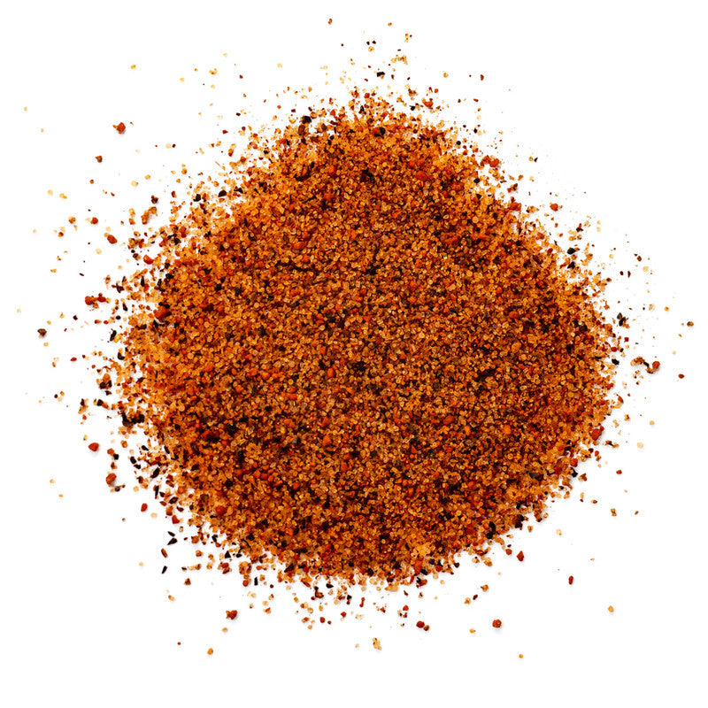 A close-up view of a pile of finely ground, reddish-brown barbecue rub with visible flecks of spices. The texture appears coarse, showcasing the blend of various seasonings.