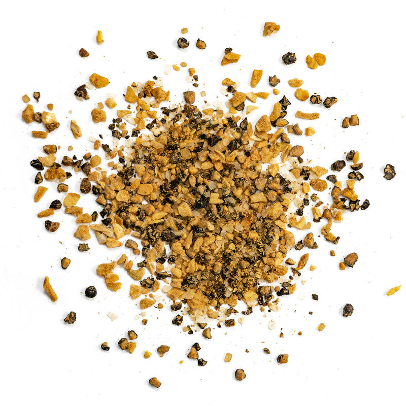 A close-up view of Killer Hogs Steak Rub powder spread out on a white surface. The seasoning consists of coarse granules, including black pepper flakes and golden-brown garlic pieces.