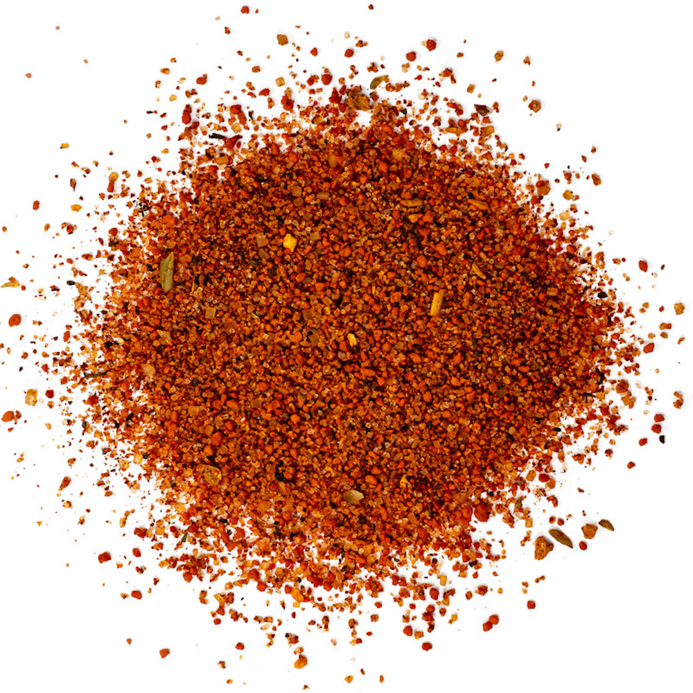 A close-up view of Killer Hogs The BBQ Rub powder spread out on a white surface. The seasoning consists of fine, coarse granules with a rich red-orange color, featuring visible spices.