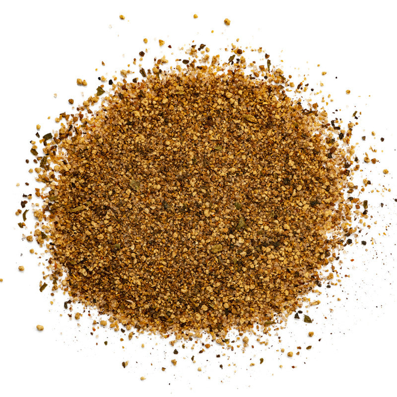 A close-up view of a pile of finely ground, brownish seasoning with visible flecks of various spices. The texture appears coarse, showcasing the blend of seasonings used in Malcom's Jammin' Jerk Caribbean Seasoning.