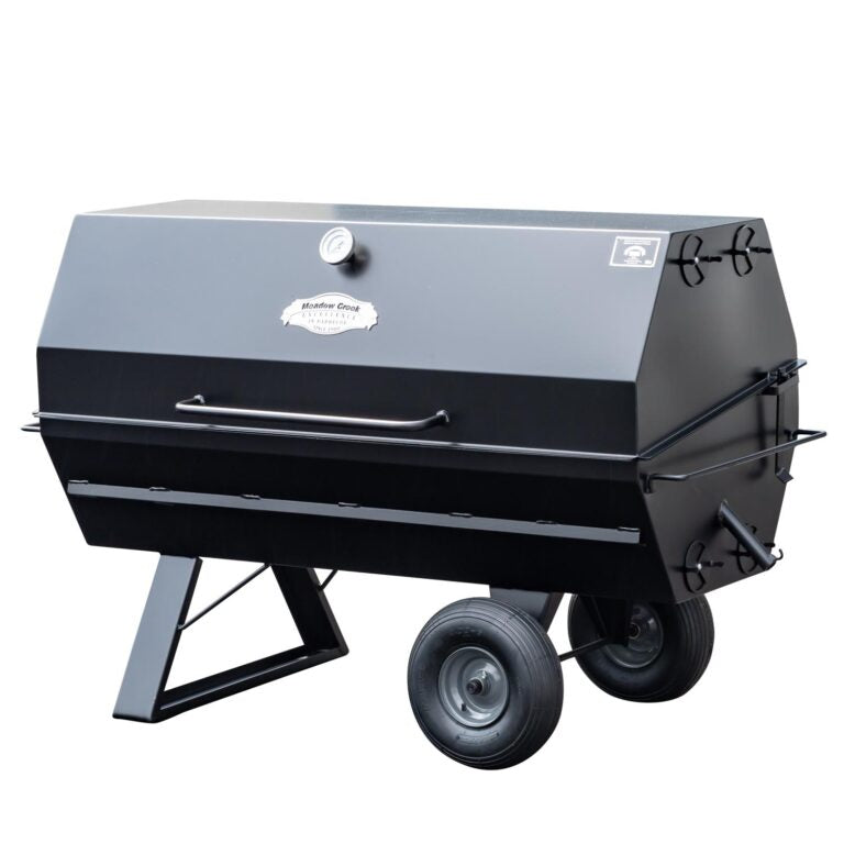 A closed Meadow Creek pig roaster with a black metal exterior, two large wheels, and a front handle for easy movement.