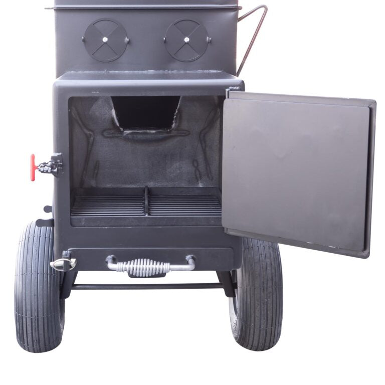 Front view of the open firebox of a Meadow Creek smoker, revealing the main cooking chamber with grates and the firebox below. The smoker has two large wheels for mobility and adjustable air vents on the door and side.