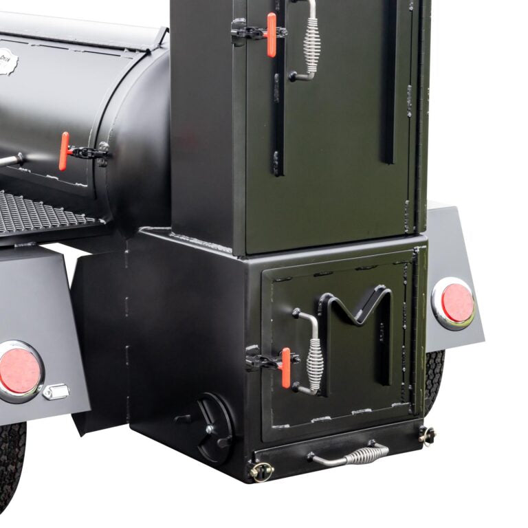 Side view of the firebox of a Meadow Creek BBQ smoker trailer, showcasing its black body and red handles.