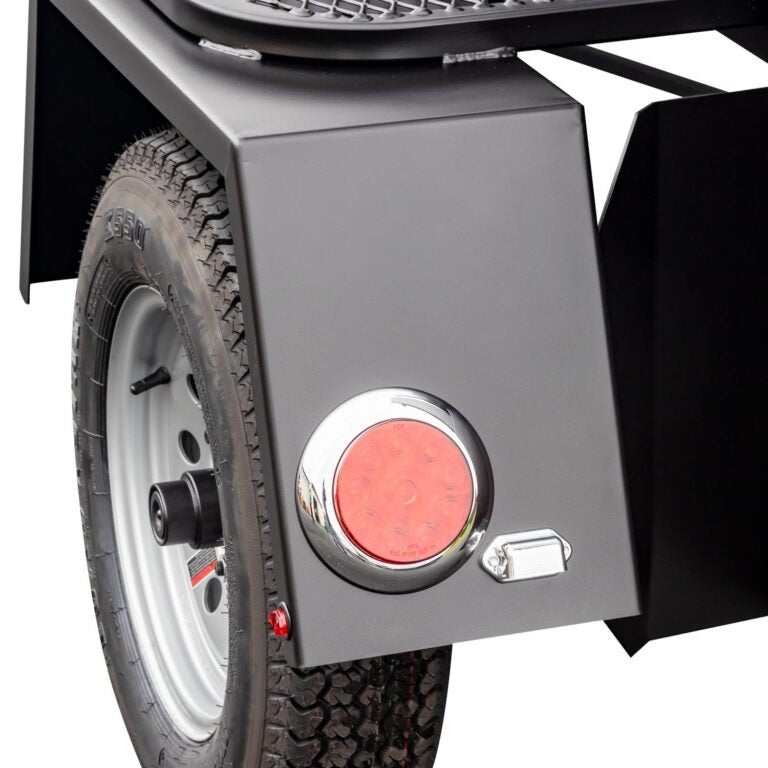 Close-up of the wheel and fender of a Meadow Creek BBQ smoker trailer, featuring a sturdy black fender and a round red reflector.