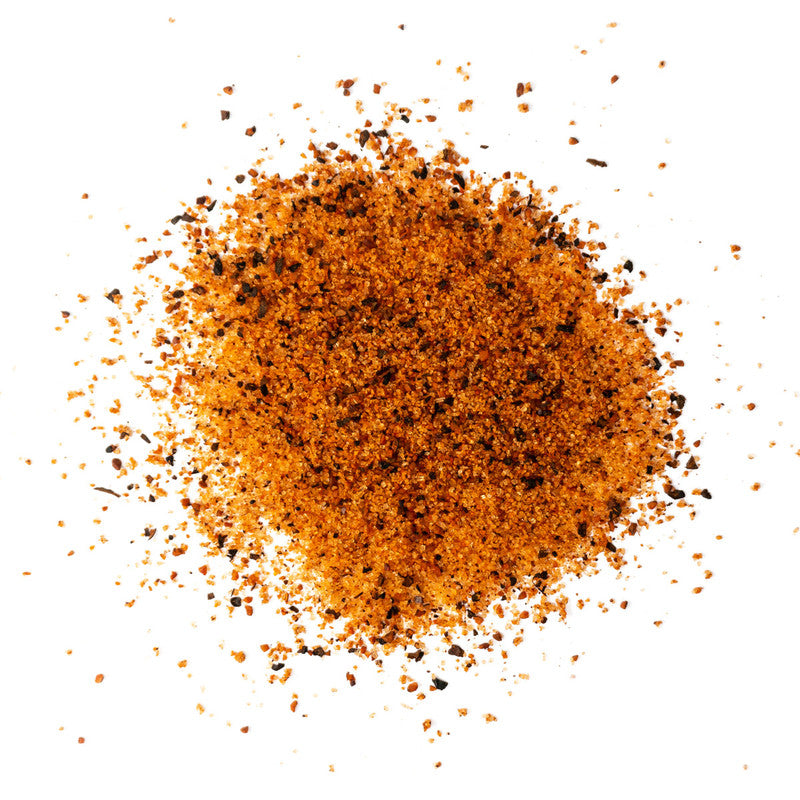 A close-up view of a pile of Meat Church Holy Gospel BBQ Rub. The spice mix is a coarse, reddish-orange powder with visible black pepper flakes.
