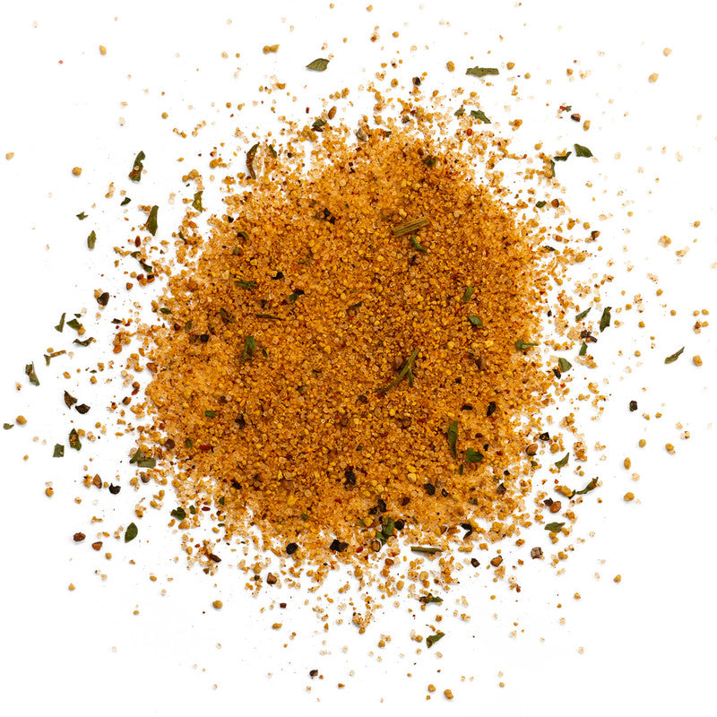 A close-up view of a pile of Meat Church Holy Voodoo Seasoning. The spice mix is a coarse, orange powder with visible green herb flakes and black pepper flakes.