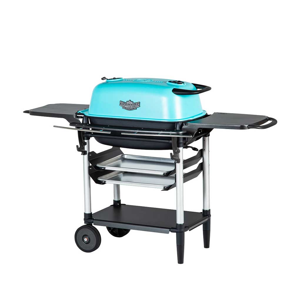 Angled view of a PK Franklin charcoal grill with a teal lid. The grill includes side shelves, two trays below the grilling area, and a lower storage shelf. One side of the grill is on wheels for easy transportation.