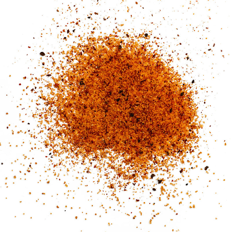 A close-up view of Plowboys BBQ Yardbird Rub seasoning blend, showing a pile of the coarse, reddish-orange spice mixture with visible flecks of various spices.