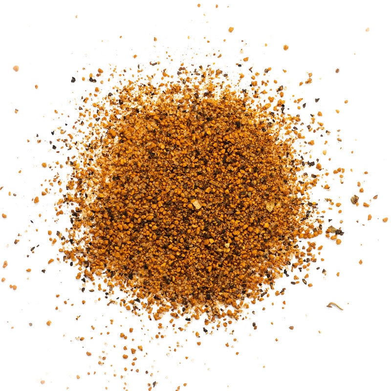 A close-up view of Plowboys BBQ Yardbird Rub, showing a mixture of coarsely ground spices with a reddish-brown color, scattered on a white background.