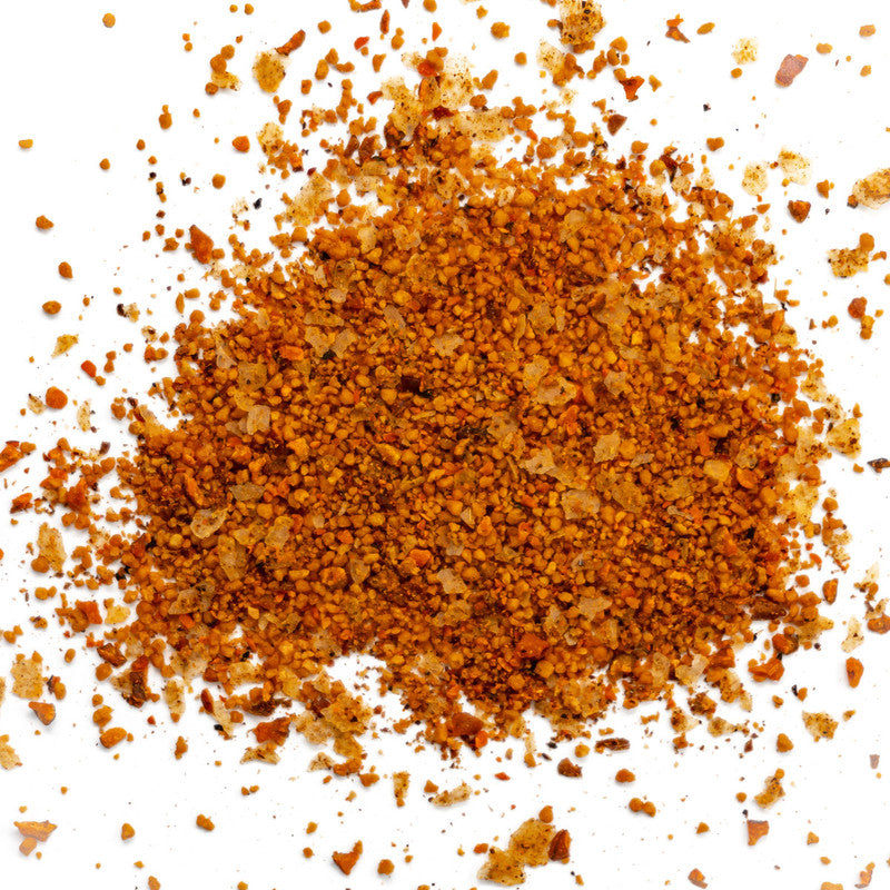 A close-up image of a pile of finely ground pecan-flavored BBQ rub with a reddish-brown color, scattered on a white background.