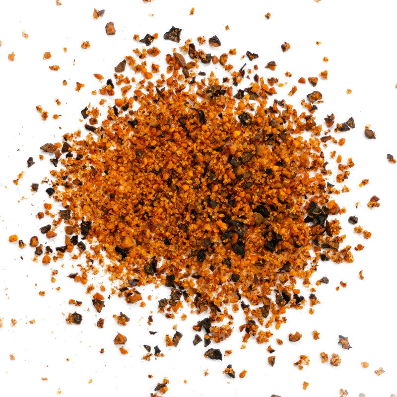 A close-up view of Simply Marvelous Peppered Cow Rub, showing a mixture of coarse orange and black granules with various spices and seasonings.