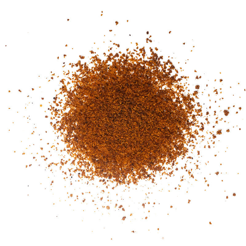 A close-up of a pile of dark reddish-brown seasoning with a coarse texture, spread out on a white surface.