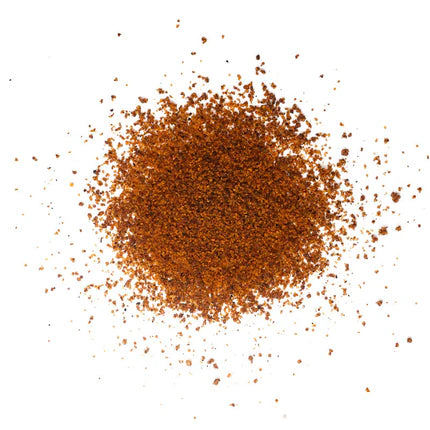A close-up view of a pile of Simply Marvelous Santa Maria Rub spice blend, showing its coarse, reddish-brown granules scattered on a white surface.