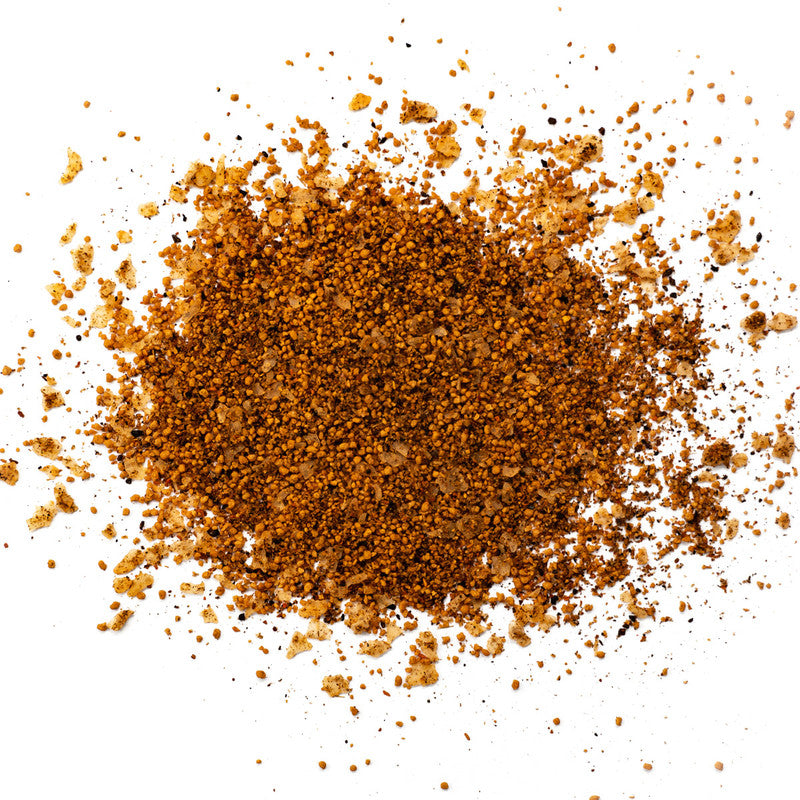 A close-up image of Simply Marvelous Spicy Apple rub. The seasoning consists of a mix of brown and beige coarse spices spread out on a white surface.