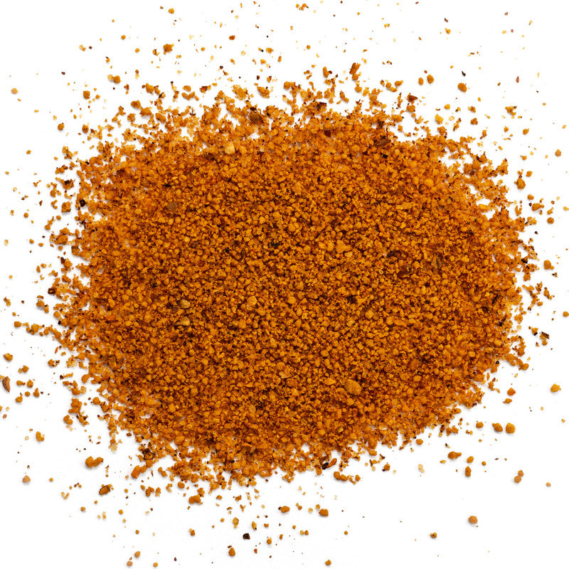 A close-up image of a pile of finely ground BBQ rub with a reddish-brown color, scattered on a white background.