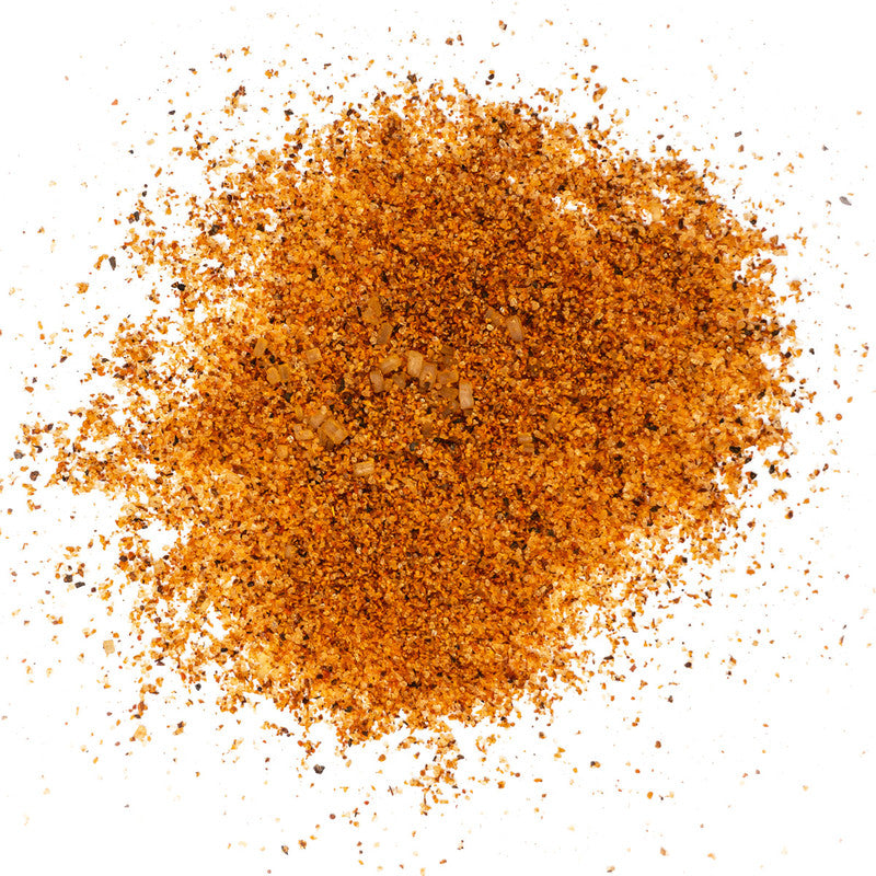 A detailed close-up of Lambert's Sweet Rub O' Mine Barbeque seasoning, showing a mix of finely ground granules in shades of orange and brown, scattered across a white surface.