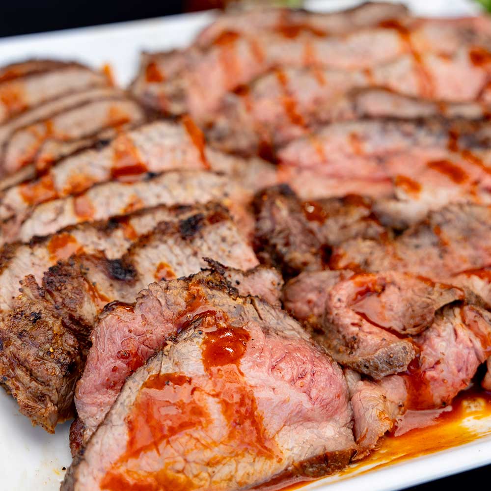 savory brisket sliced and displayed on a white plate, seasoned with sweet money hot barbecue seasoning and drizzled with hot sauce