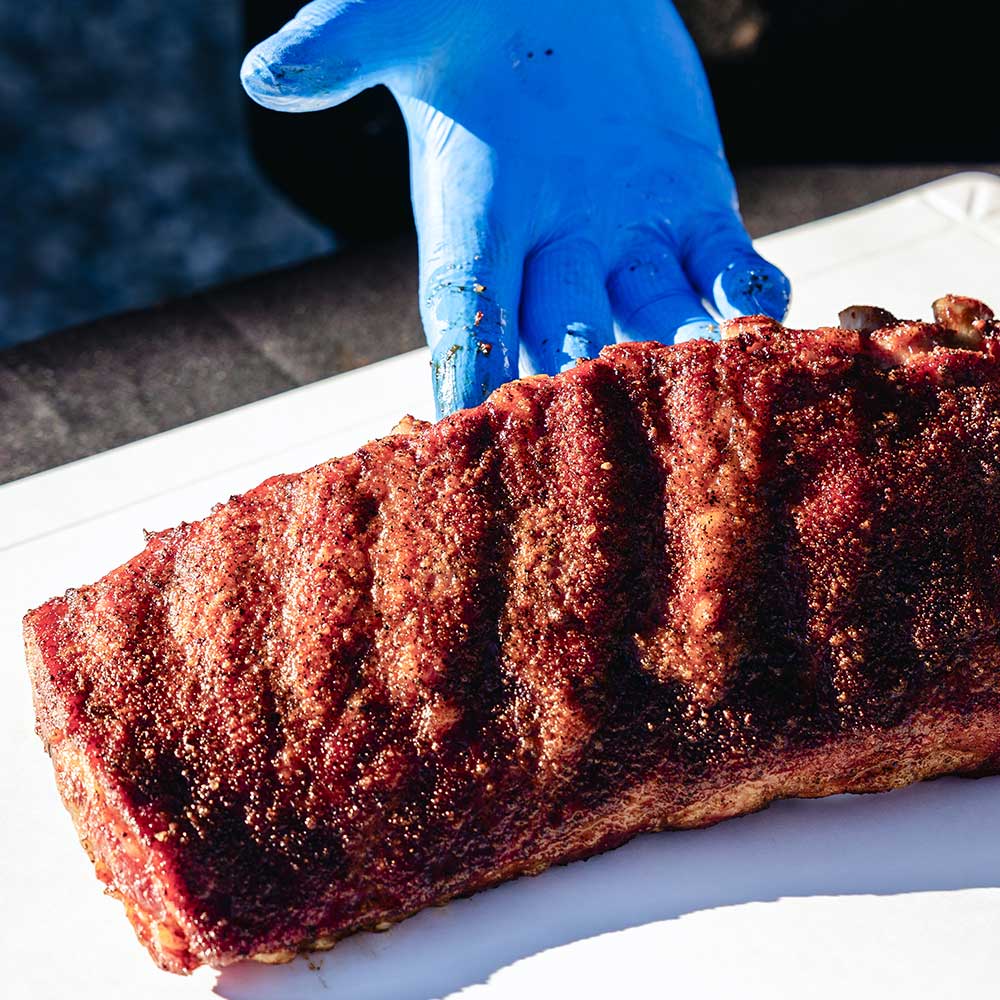 gloved hand lifting up and displaying deliciously seasoned ribs, encrusted with an enticing texture of barbecue seasonings