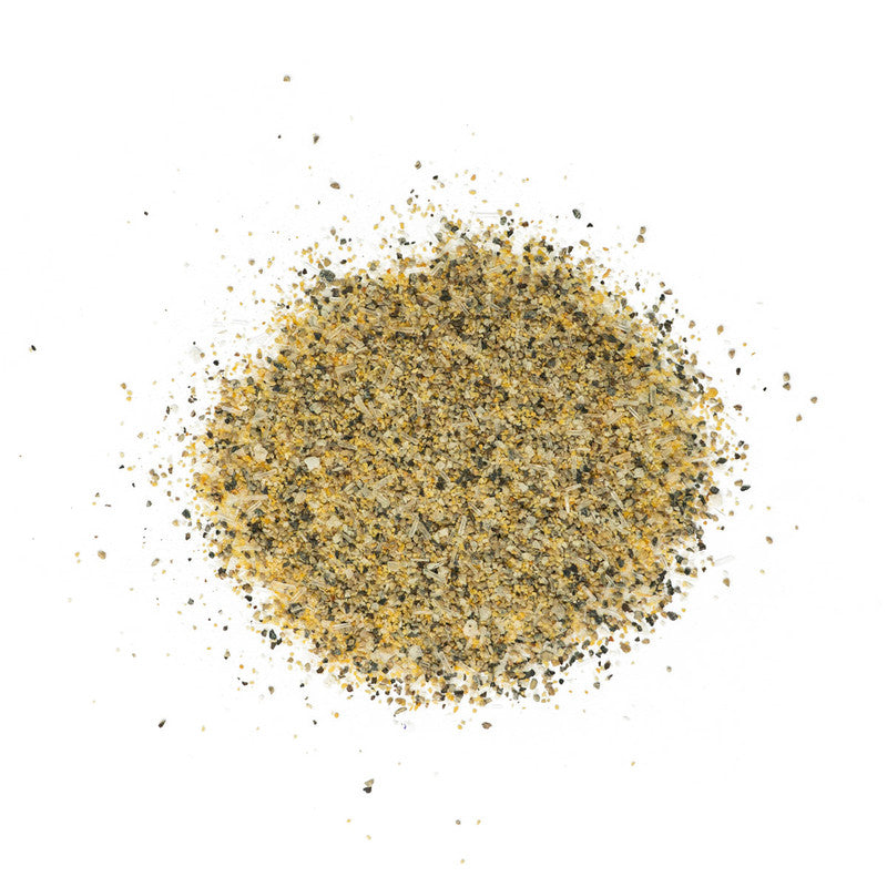 A close-up view of a scattered pile of Tuffy Stone The Big Umami All Purpose Mix on a white background. The mix has a coarse texture with a blend of yellow, black, and white spices.