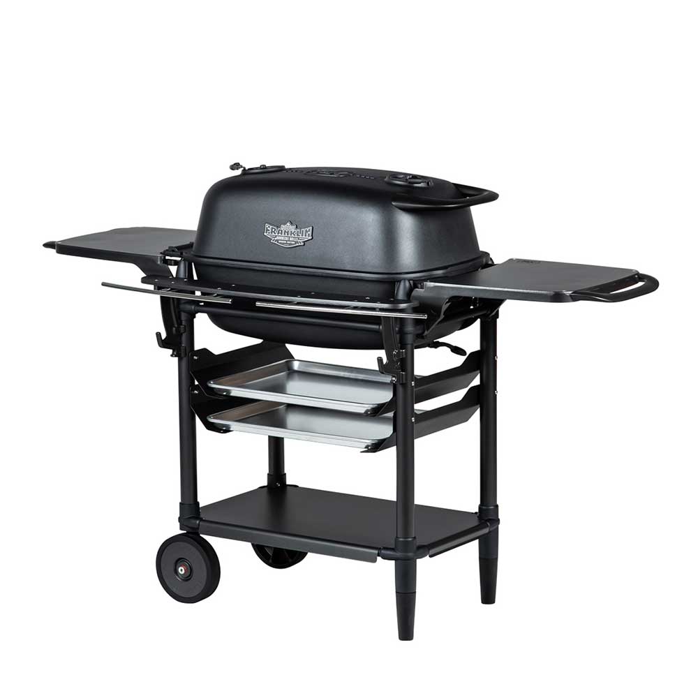 Angled front view of a PK Franklin charcoal grill with a black lid. The grill features side shelves, two trays beneath the grilling area, and a lower shelf for additional storage. One side of the grill is supported by two wheels for easy mobility.