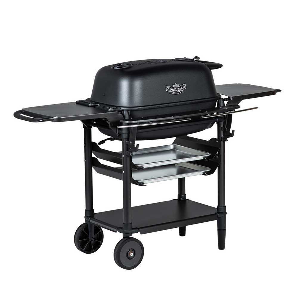 Angled view of a PK Franklin charcoal grill with a black lid. The grill includes side shelves, two trays below the grilling area, and a lower storage shelf. One side of the grill is on wheels for easy transportation.