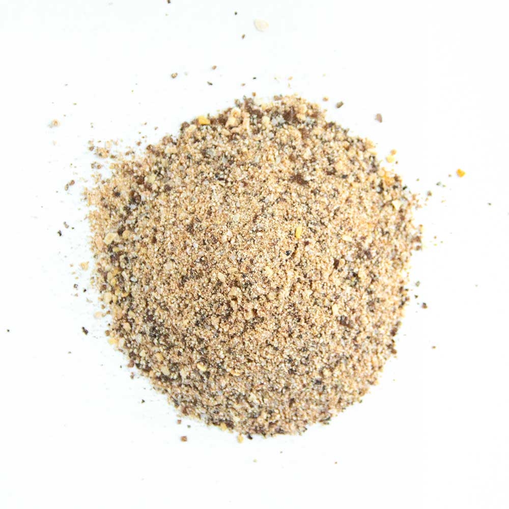 Close-up view of a beige and brown mixed seasoning pile, consisting of coarse salt, herbs, and spices, displayed on a white background.