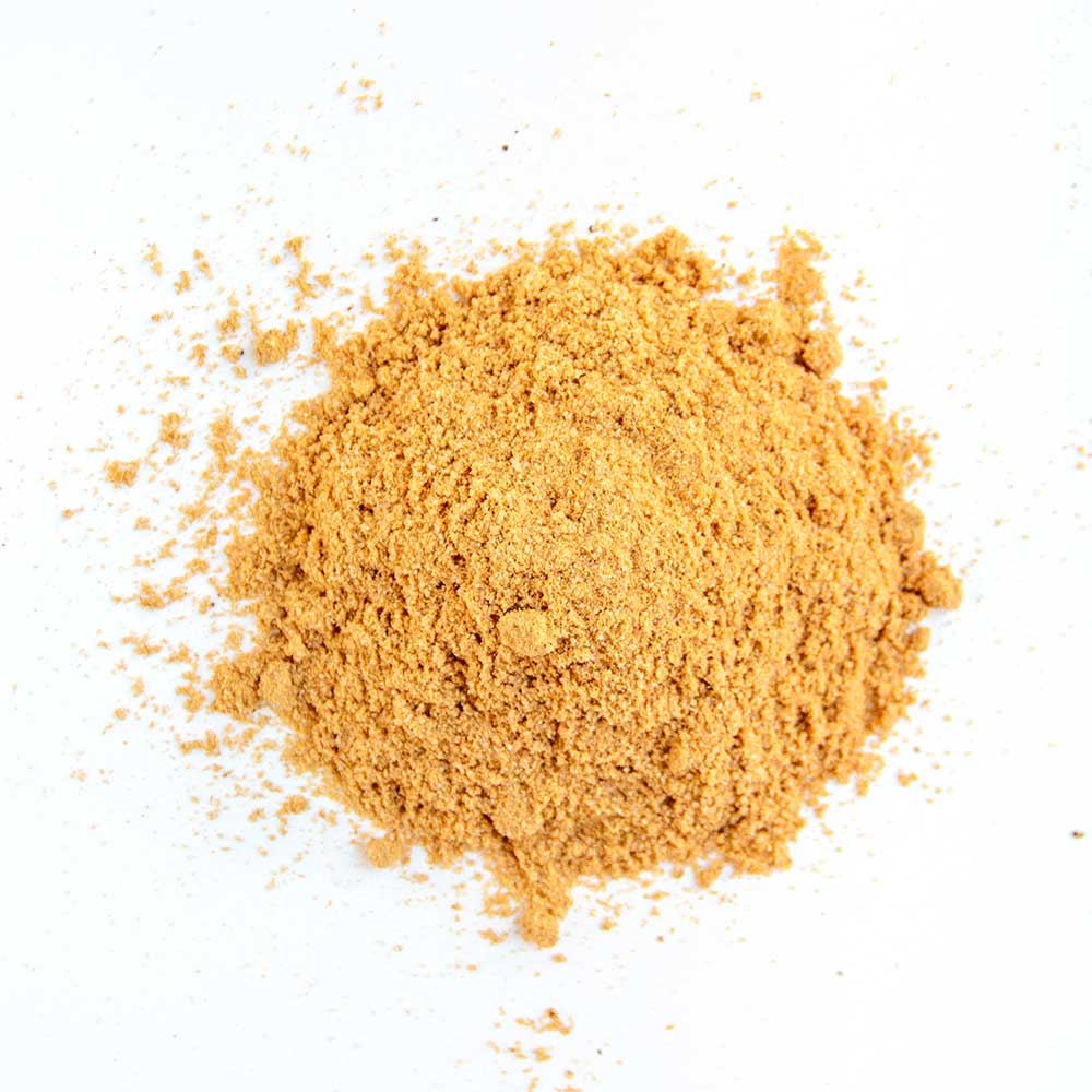 A close-up of fine golden-yellow seasoning powder, spread loosely on a white background, showing a mix of spices optimized for poultry.